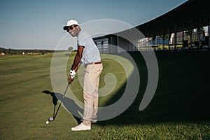 African american man playing golf with club and ball at green lawn