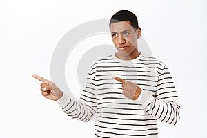 African american man pointing and looking left with disappointing look, standing over white background