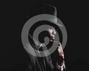 African american man posing against a black background wearing a suit and hat looking mindful and sad.Grieving person