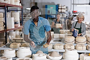 African american man prepares pottery with foam sponge - removes roughness and unevenness