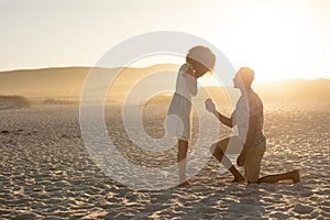An African American man proposing to the woman on beach on a sunny day