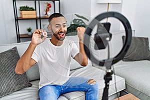 African american man recording vlog tutorial about bitcoin with smartphone at home screaming proud, celebrating victory and