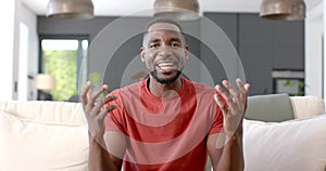 African American man in a red shirt sits comfortably on a couch on video call