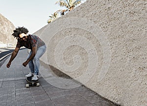 African american man riding longboard on the road with palm trees in the background - Focus on face