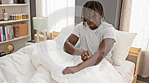 African american man scratching arm for itchy sitting on bed at bedroom