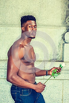 Young black man holding white rose, standing outdoors in New York City, looking away