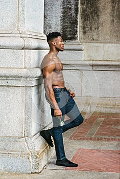 Young black man holding white rose, standing outdoors in New York City, looking forward, thinking