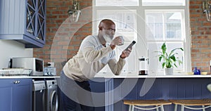 African american man senior man drinking coffee and using smartphone at home