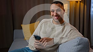 African american man sit on sofa in living room using online mobile application ethnic man playing game on phone