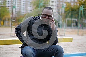 African american man sits at sport ground and speaks on smartphone