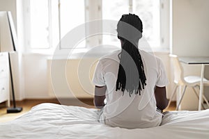 African American Man Sitting On Bed And Looking At Window, Rear View