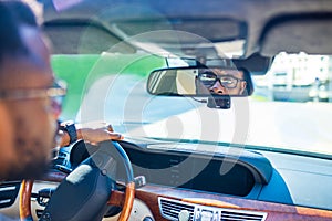 african american man sitting in a car and adjusting rearview mirror looking to back