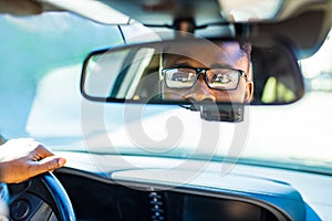 african american man sitting in a car and adjusting rearview mirror looking to back