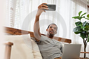 African American man sitting on couch doing online video chat on smartphone