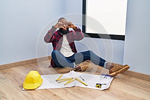 African american man sitting on the floor at new home looking at blueprints smiling in love doing heart symbol shape with hands