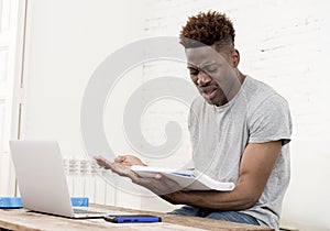 African american man sitting at home living room working with laptop computer and paperwork