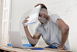 African american man sitting at home living room working with laptop computer and paperwork