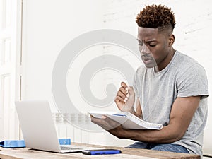 African american man sitting at home living room working with laptop computer and paperwork