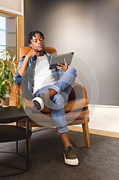 African American man sitting in a modern business office, holding a tablet, looking thoughtful