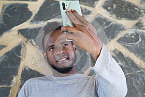 African-American man sitting on a a park bench taking a selfie with his mobile phone. He is looking at the camera very happy and
