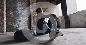 African american man sitting resting after exercising with medicine ball in an empty urban building