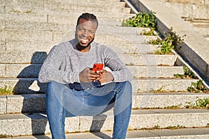 African American man sitting on stairs smiling, looking at camera, on a sunny day. Happy young Latino man. Concept of