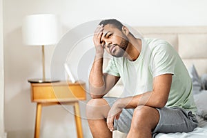 African american man sitting in thoughtful pose on edge of bed