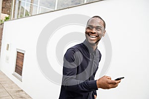 African American man smiling with mobile phone in hand while walking outside