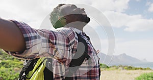 African american man standing with arms wide open while trekking in the mountains