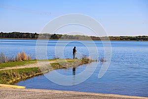 An African American man standing on the banks of the lake fishing with vast blue lake water