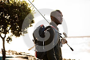 African American man standing outside with fishing rod and bag