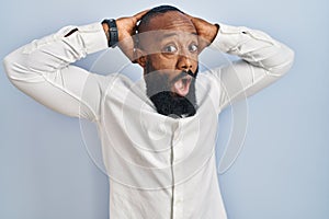 African american man standing over blue background crazy and scared with hands on head, afraid and surprised of shock with open