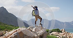 African american man standing on rock with arms wide open while trekking in the mountains