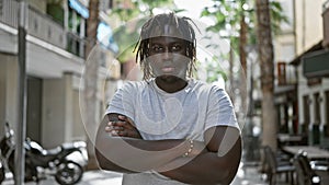 African american man standing with serious expression and arms crossed gesture at street