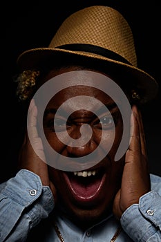 African-American man in a straw hat holds his head in his hands with his mouth open from shock