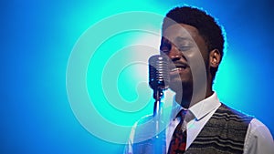 African American man in a stylish suit sings a song into a retro microphone. The jazz vocalist performs in a dark studio