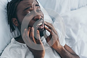 African american man suffering from jaw pain in bedroom