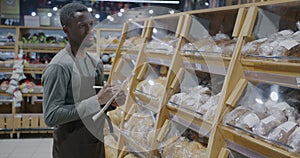 African American man supermarket manager counting bread and writing doing inventory in retail store