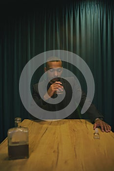 African American man at a table drinking whiskey with a glass of wine. background green curtain.