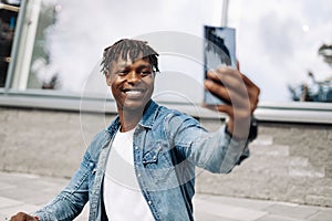 African American man takes a selfie on the street, in front of a glass building, traveling alone