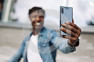 African American man takes a selfie on the street, in front of a glass building, traveling alone, phone close-up