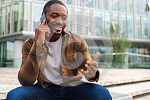 African american man talking on smartphone on street in city outdoor. Man with cell phone chatting with friends. Smiling