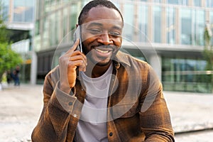 African american man talking on smartphone on street in city outdoor. Man with cell phone chatting with friends. Smiling