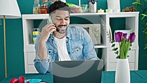 African american man talking on smartphone using laptop at dinning room