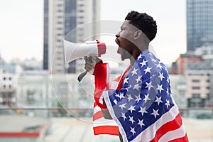 African-American man with the USA flag shouts in a megaphone and protests against the background of the city, black lives matters