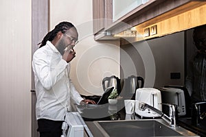 African American man using digital tablet at the kitchen reading social media internet, typing text or shopping online