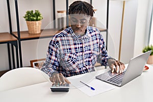 African american man using laptop and calculator accounting at home