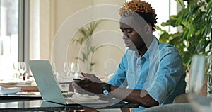 African american man using laptop computer in cafe call by mobile phone