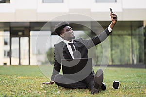 African-American man using laptop outdoors, sitting on the grass near office