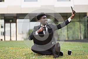 African-American man using laptop outdoors, sitting on the grass near office
